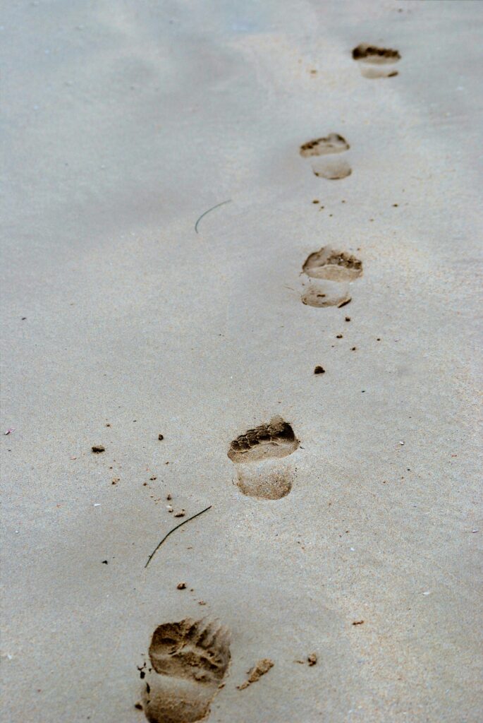A serene view of footprints leading across soft sand on a calm, empty beach.